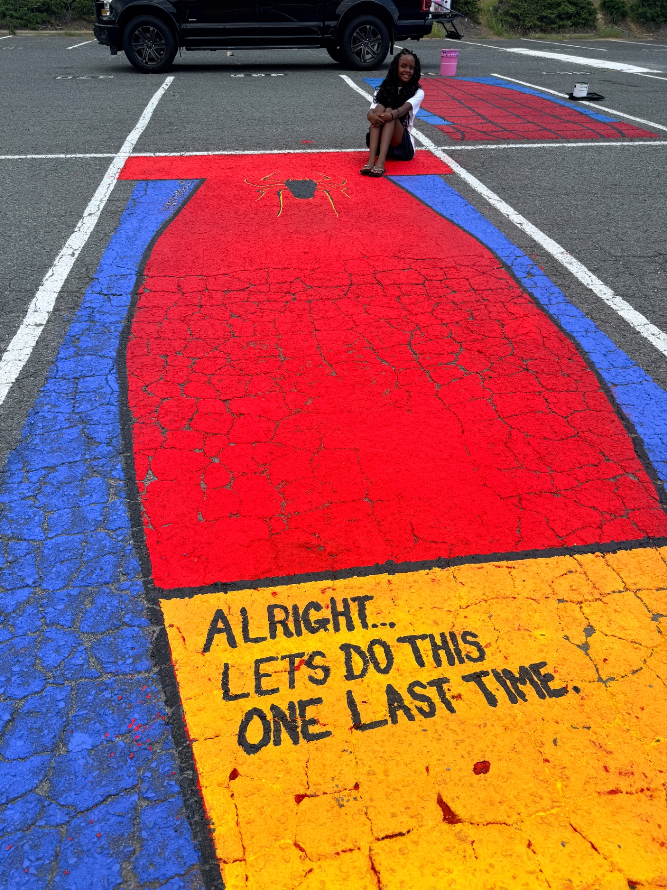 Anabelle sitting on the finished Spider-Man-inspired parking-space mural with the painted quote below